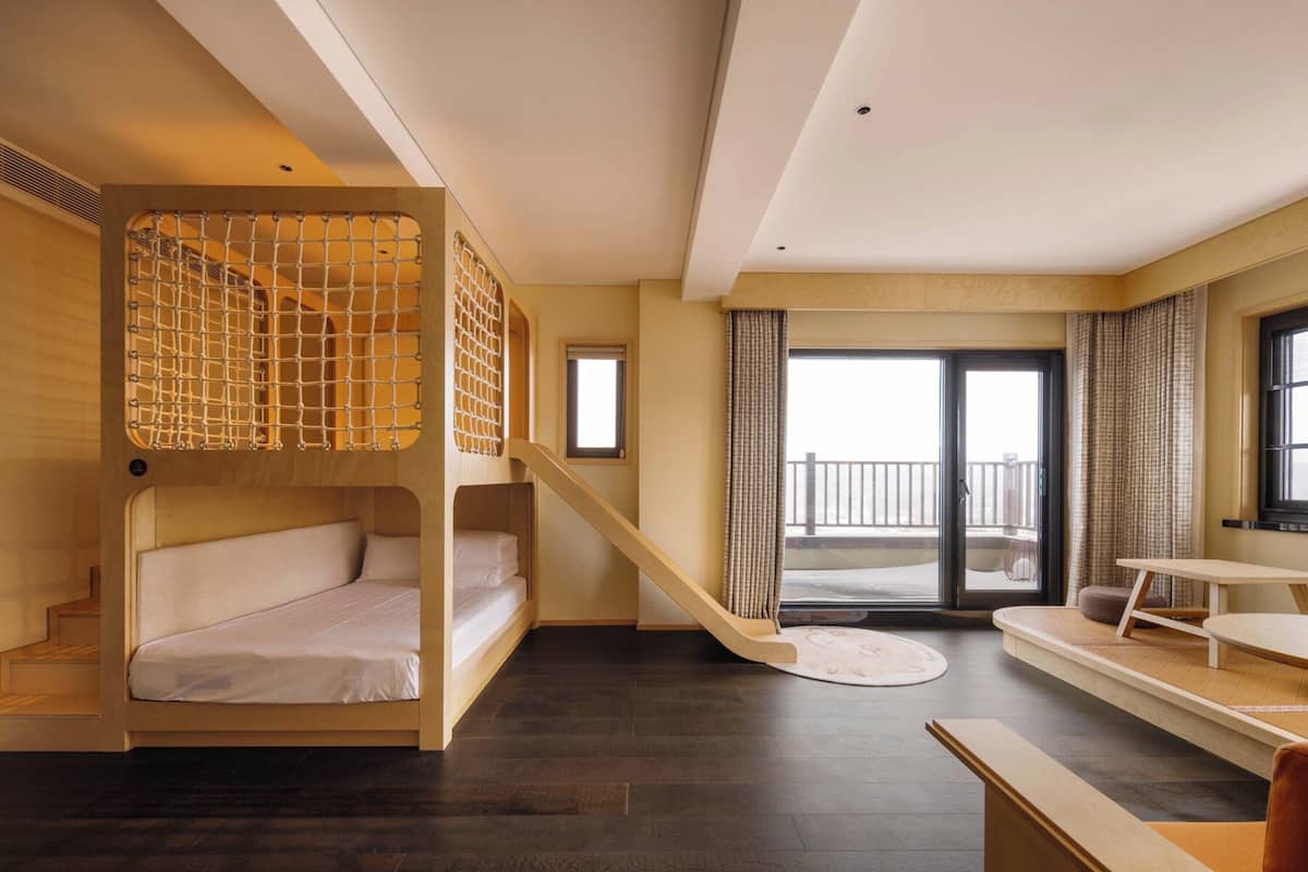 Ein Zimmer mit einem Etagenbett, einer Treppe, einer Essecke und Blick ins Freie.