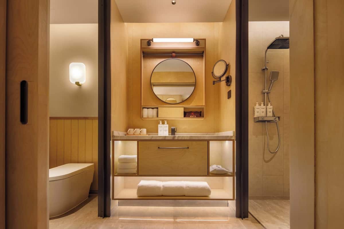Ein modernes Badezimmer mit Waschtisch aus Holz, einem runden Spiegel, einem Handtuchhalter und einer Dusche.