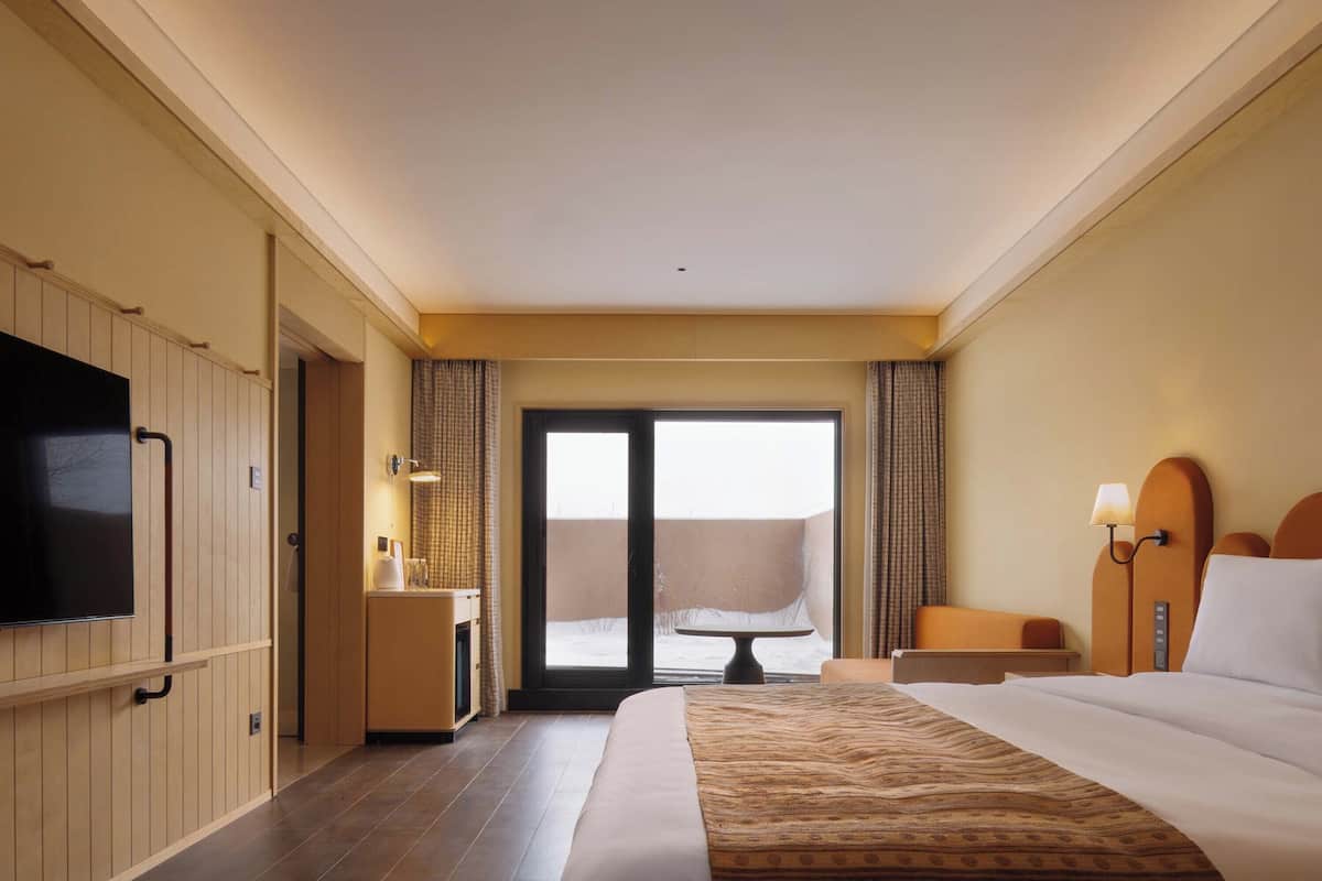 Ein Hotelzimmer mit einem großen Bett, einem Flachbildfernseher, einem Schreibtisch mit Lampe und Blick ins Freie.