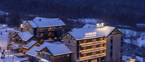 A hotel with multiple buildings, including a main building with balconies and a smaller annex. There are signs indicating the hotel name and a restaurant.