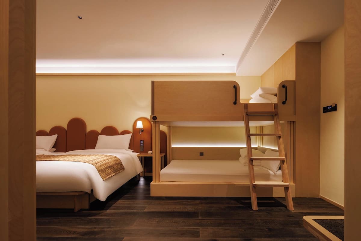 Ein Hotelzimmer mit zwei Betten, einem Etagenbett, einer Holzleiter und einem Nachttisch mit einer Lampe.