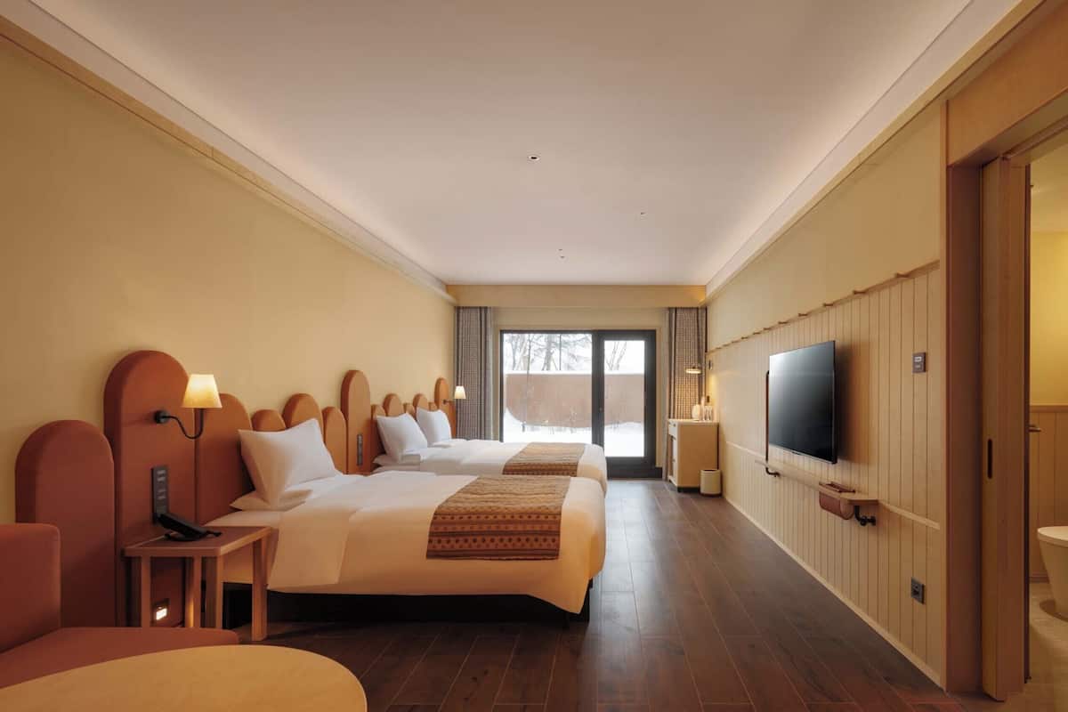 Ein Hotelzimmer mit zwei Betten, einem Fernseher, einem Schreibtisch und einem Badezimmer.