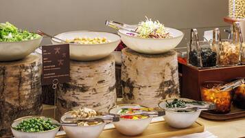 A buffet table with various dishes, including green peas, bell peppers, and other vegetables, served on birch tree trunks.