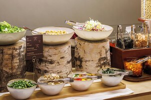 A buffet table with various dishes, including green peas, bell peppers, and other vegetables, served on birch tree trunks.