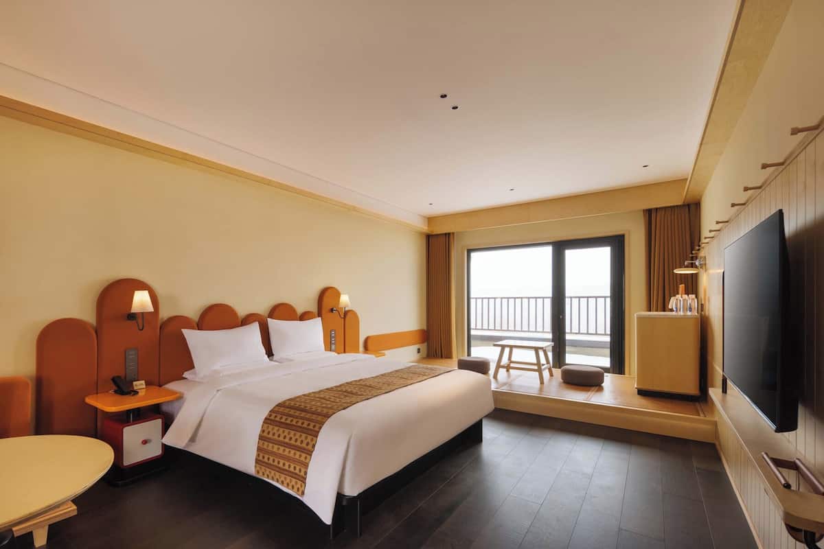 Ein Hotelzimmer mit einem großen Bett, einem Fernseher, einem Schreibtisch und einem Balkon mit Blick.