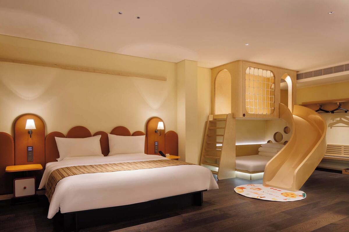 Ein Hotelzimmer mit einem großen Bett, einer eingebauten Rutsche und einer kleinen Sitzecke mit Stadtblick.