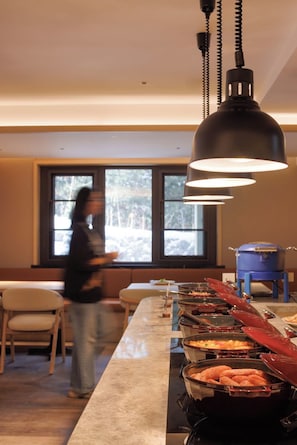 Montaje de bufé con diferentes alimentos, un ventanal con vista a árboles y una persona en movimiento.