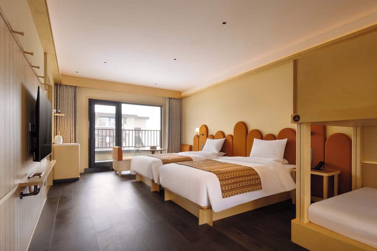 Ein Hotelzimmer mit zwei Betten, einem Fernseher, einem Schreibtisch und einem Balkon mit Aussicht.