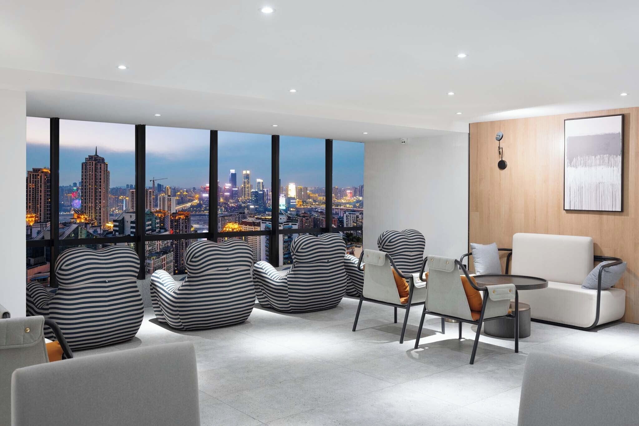 Una sala de estar moderna con ventanas amplias que ofrecen vista a la ciudad, sillones tipo saco a rayas, una mesa redonda y un sofá.