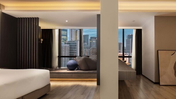 Una habitación de hotel moderna con una cama grande, vistas de la ciudad y una zona de estar también con vistas.