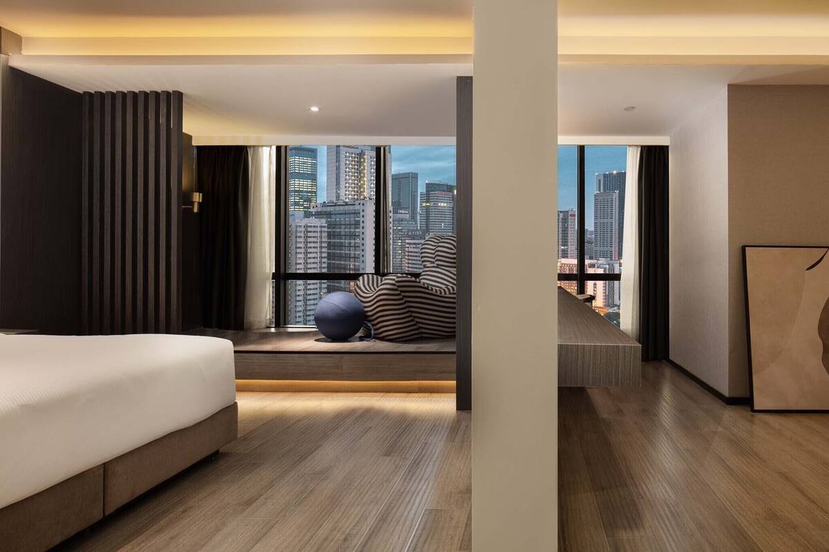 Una habitación de hotel moderna con una cama grande, vistas de la ciudad y una zona de estar también con vistas.