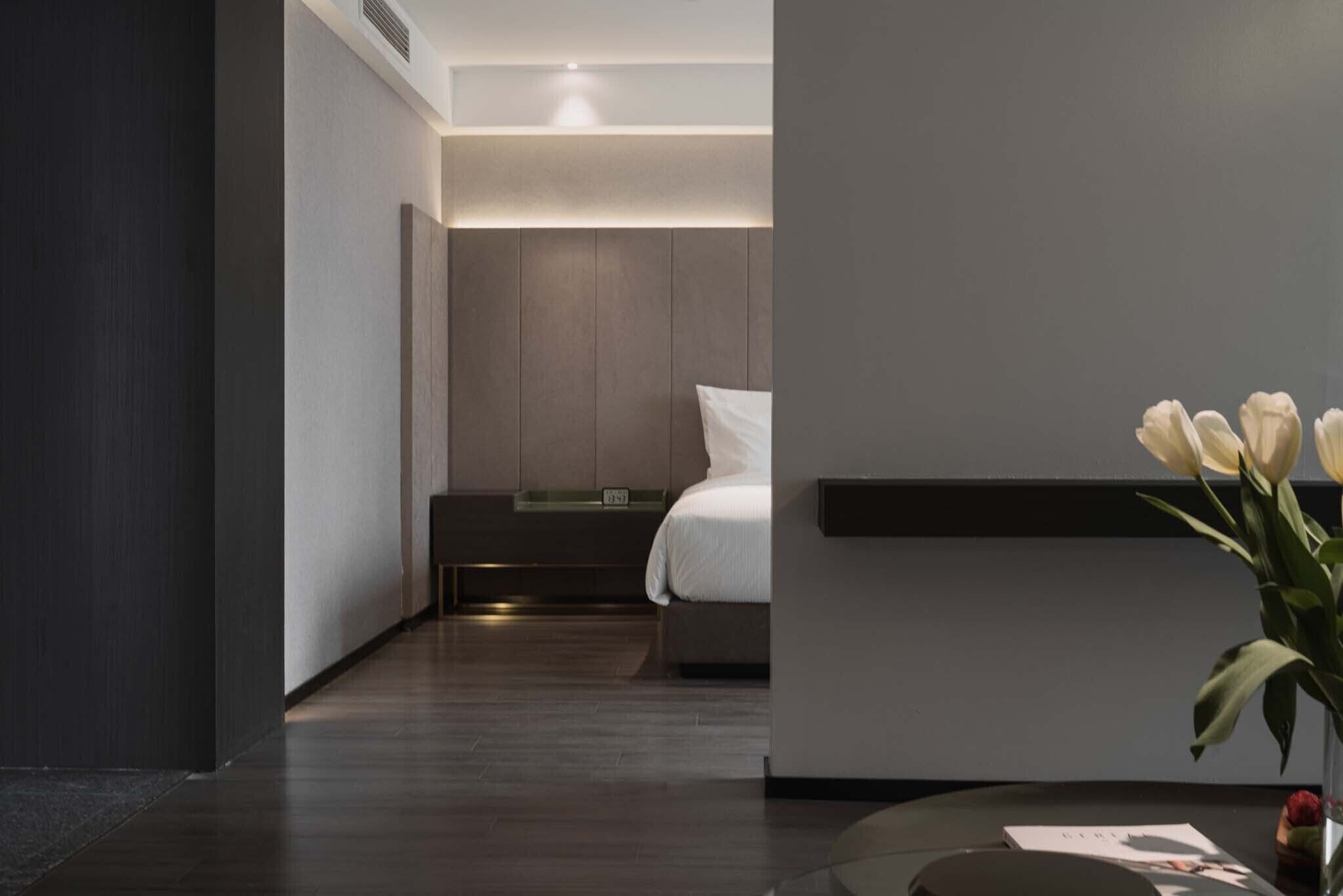 A modern hotel room with a bed, bedside table, and a vase of flowers.