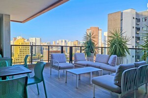 Una terraza en la azotea con vistas a la ciudad, amueblada con un sofá, sillas y una mesa.