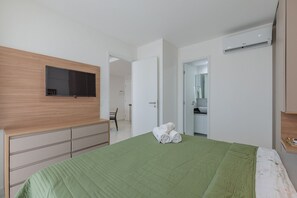 A bedroom with a green bedspread, a wooden dresser, a flat-screen TV, and a wall-mounted air conditioner. - Jsmart Studio #1106 - Comfortable apt by Carpediem (Fortaleza)