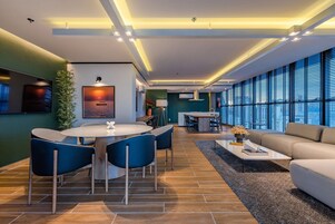 Una sala de estar moderna con una mesa de comedor redonda, sillas azules, un sofá beige y un ventanal con persianas.