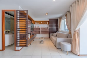 Ein modernes Wohnzimmer mit einer Couch, einem Hocker und einem Holzregal mit Dekorationselementen.