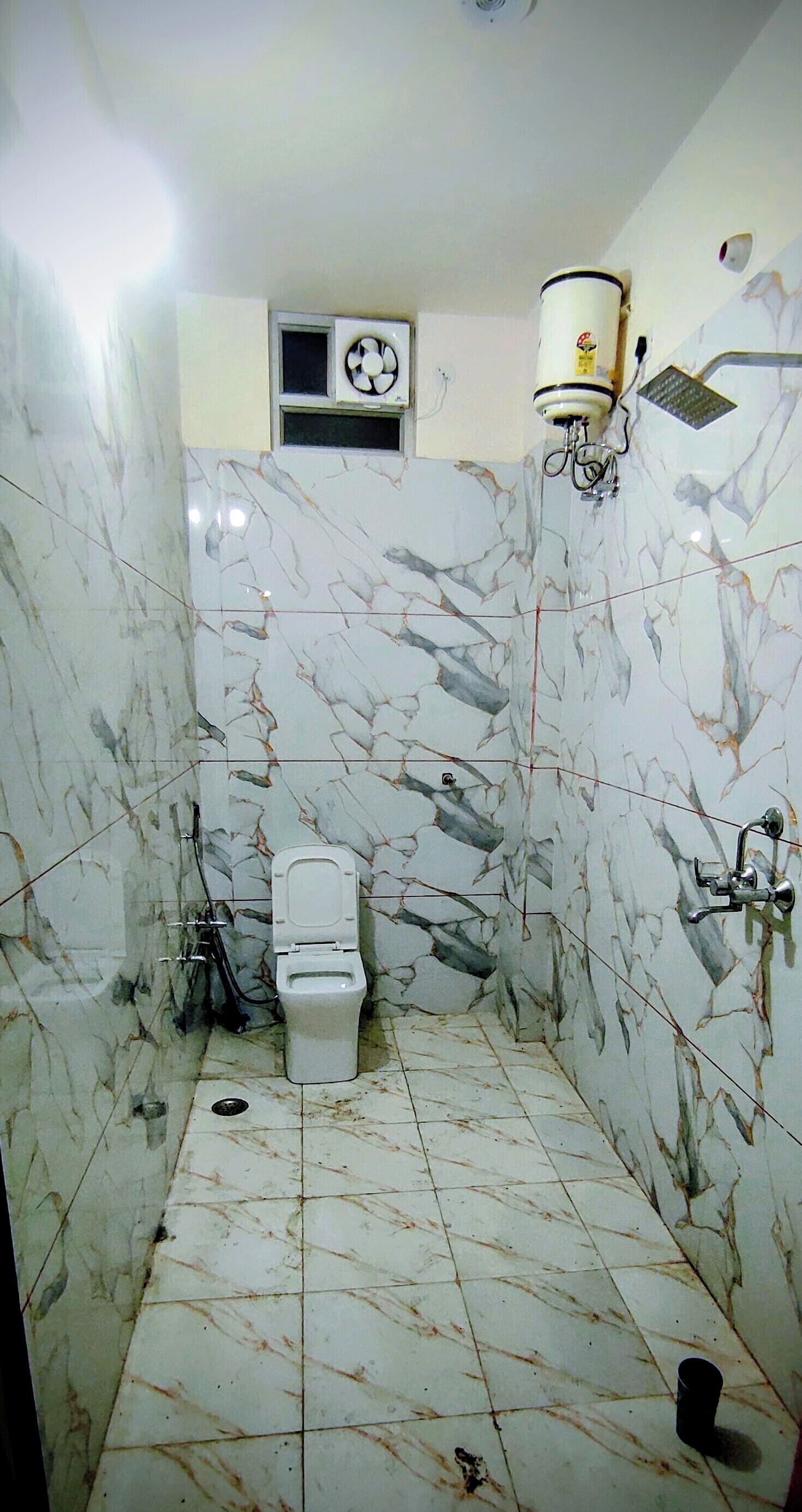 Casa de banho com sanita, paredes de mármore e ventoinha no teto.