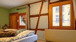 Une pièce avec un lit, un radiateur, une fenêtre donnant sur des immeubles et une porte.