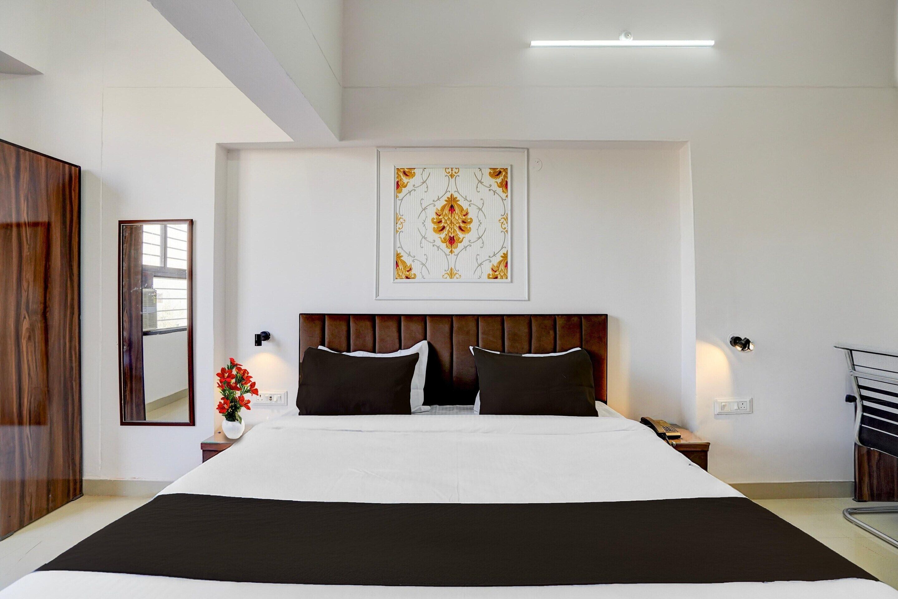 A hotel room with a large bed, a headboard, a bedside table, a mirror, and a wall-mounted artwork.