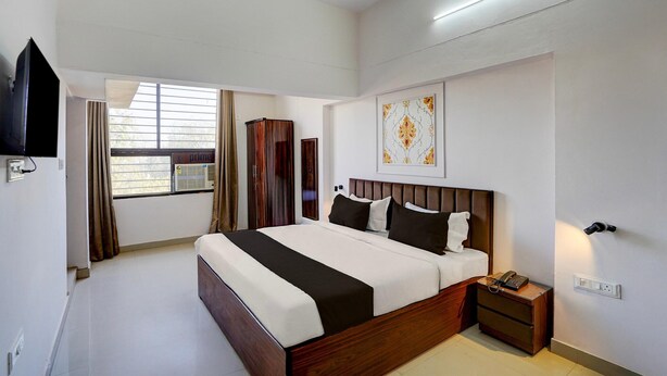 Ein modernes Hotelzimmer mit einem großen Bett, einem Fernseher, einem Kleiderschrank und einem fenster mit Vorhängen.