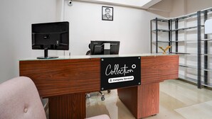Ein Empfangstresen mit einem Schild, auf dem 'Collection Company-Serviced' steht, ein gerahmtes Porträt an der Wand und ein Metallregal rechts.