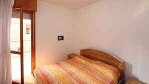 Une chambre à coucher avec un lit en bois, une table de chevet, une petite table et une porte coulissante donnant sur un balcon.