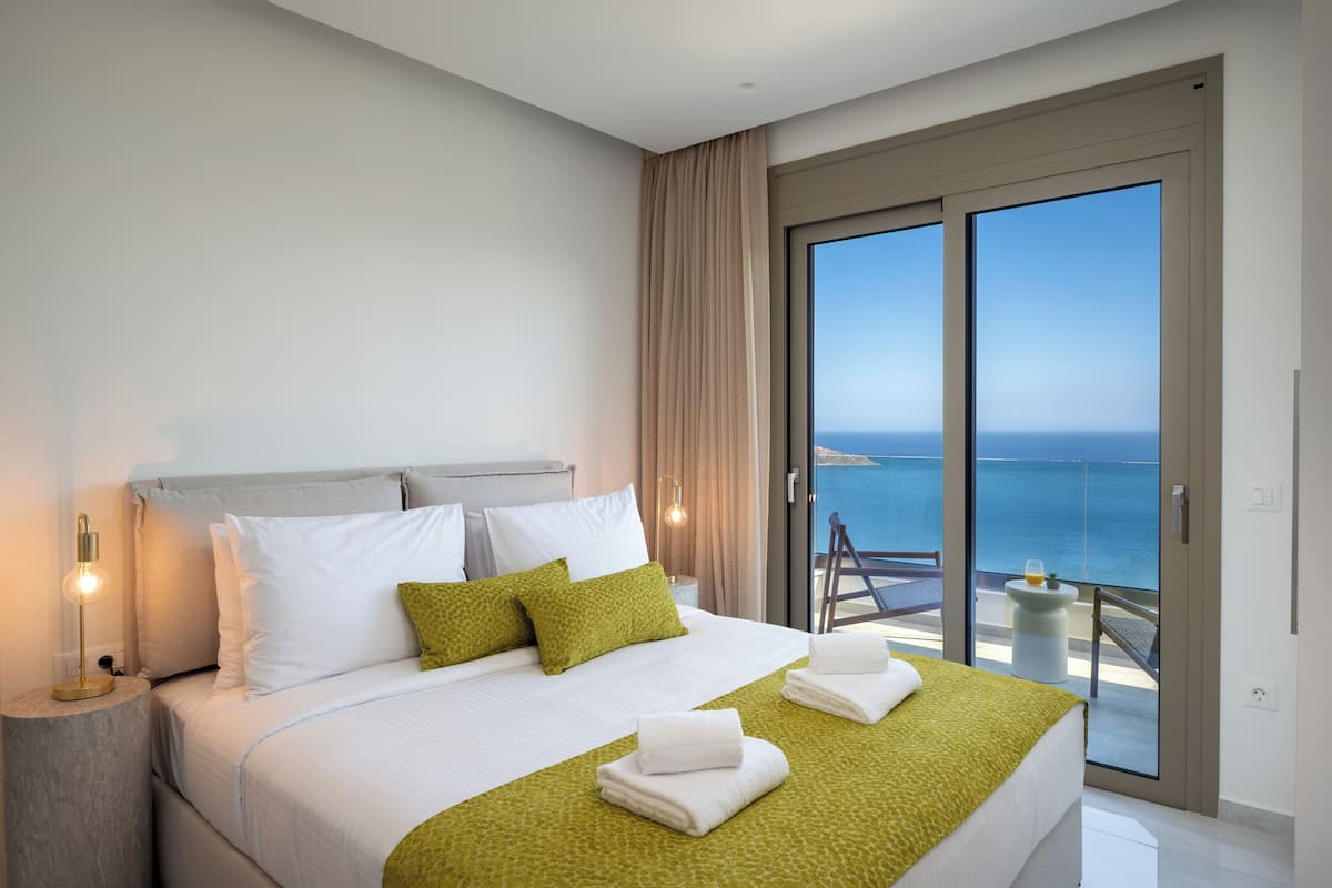 Une chambre d’hôtel moderne dotée d’un grand lit, d’un balcon avec vue sur la mer et d’un éclairage soigné.