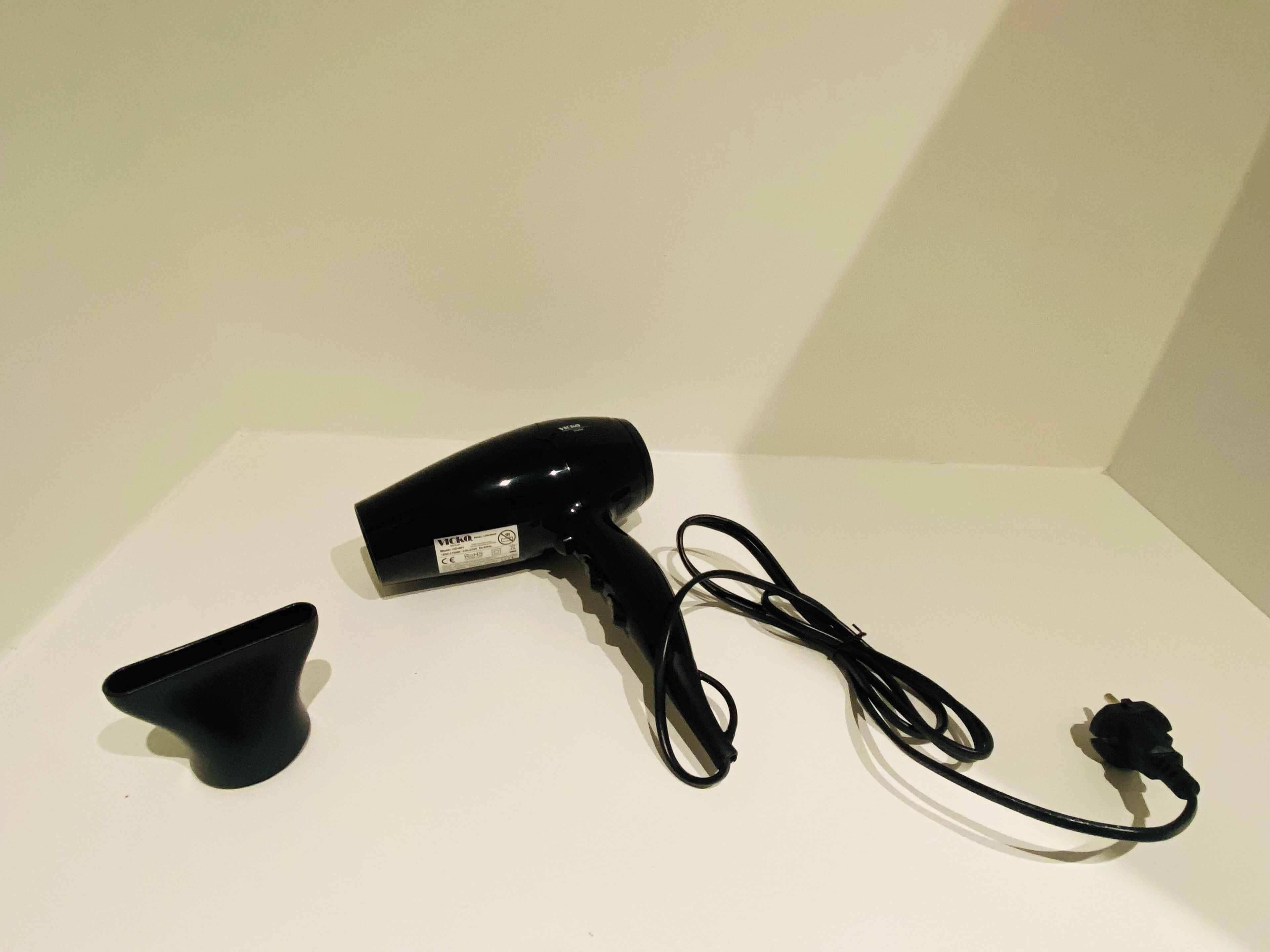 A black hairdryer with a plug and a black stand on a white surface.