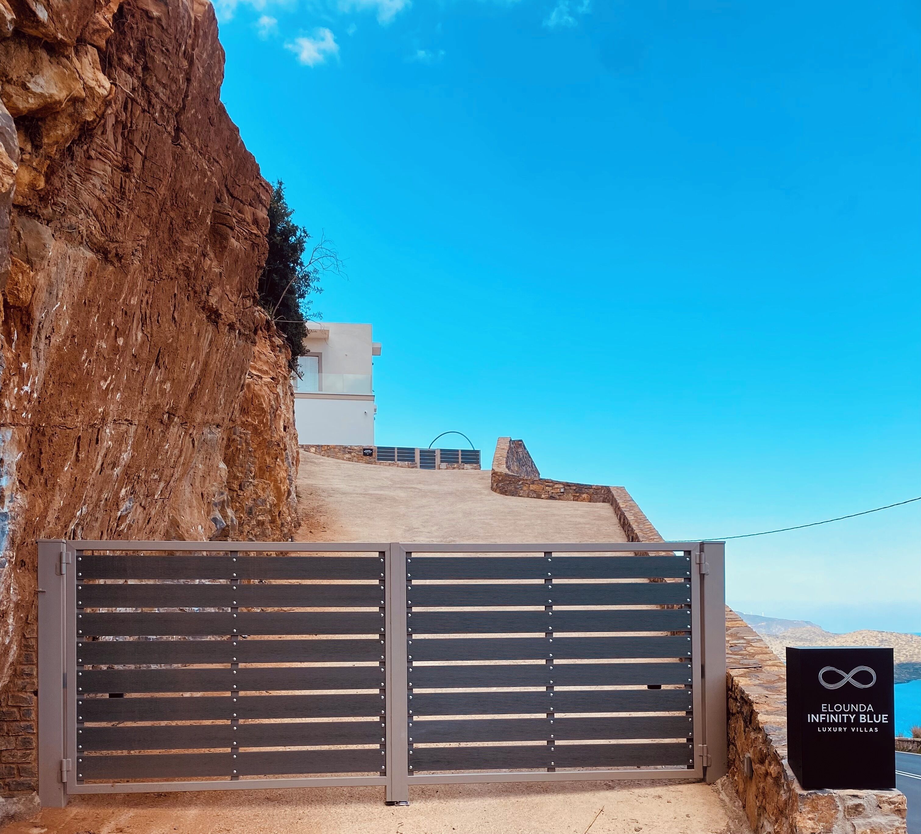 A gated entrance to a property with a clear view of a modern building and a mountainous landscape.