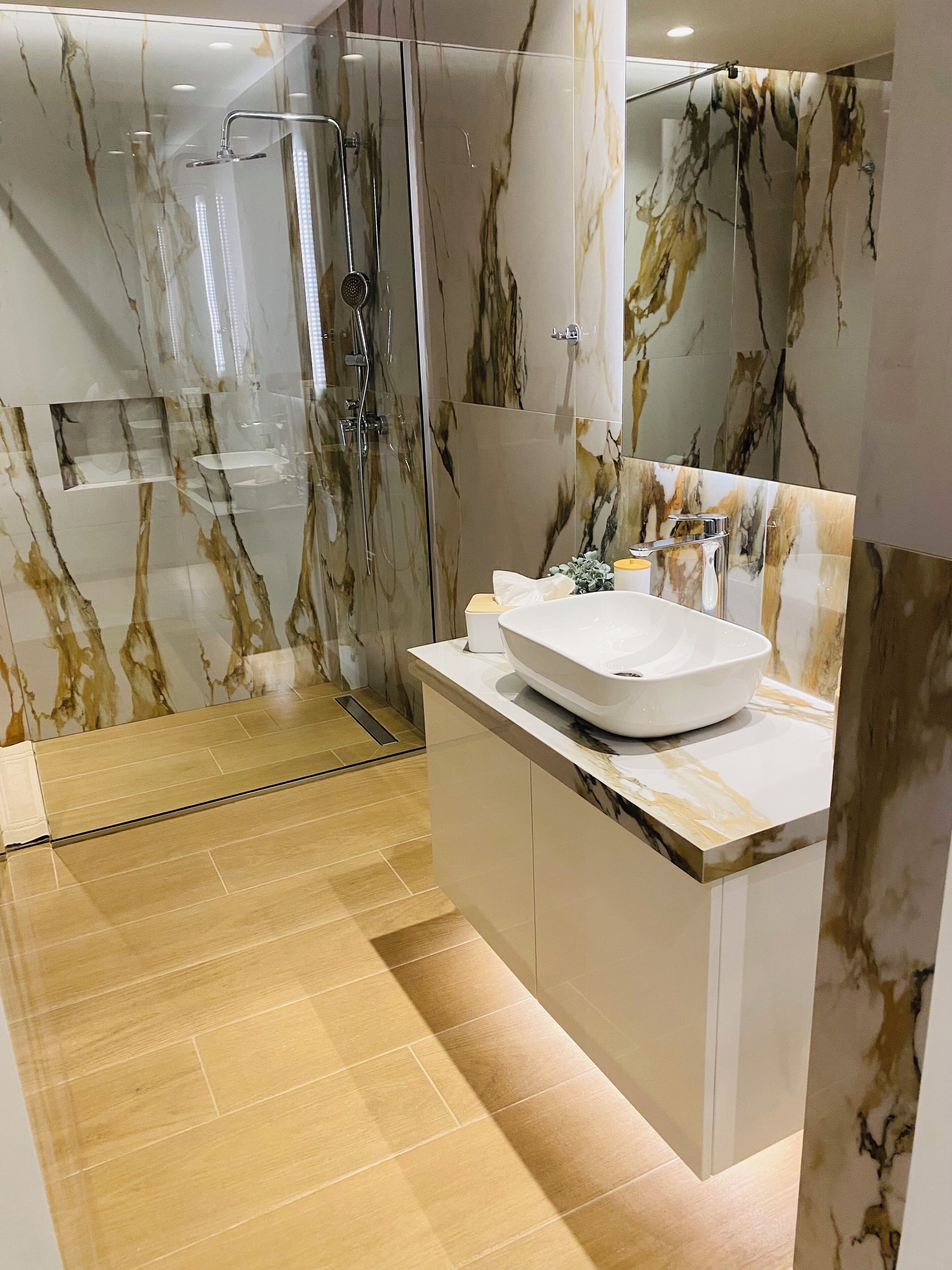 Une salle de bain moderne avec une douche à parois de verre, un lavabo blanc et des murs à motifs de marbre.