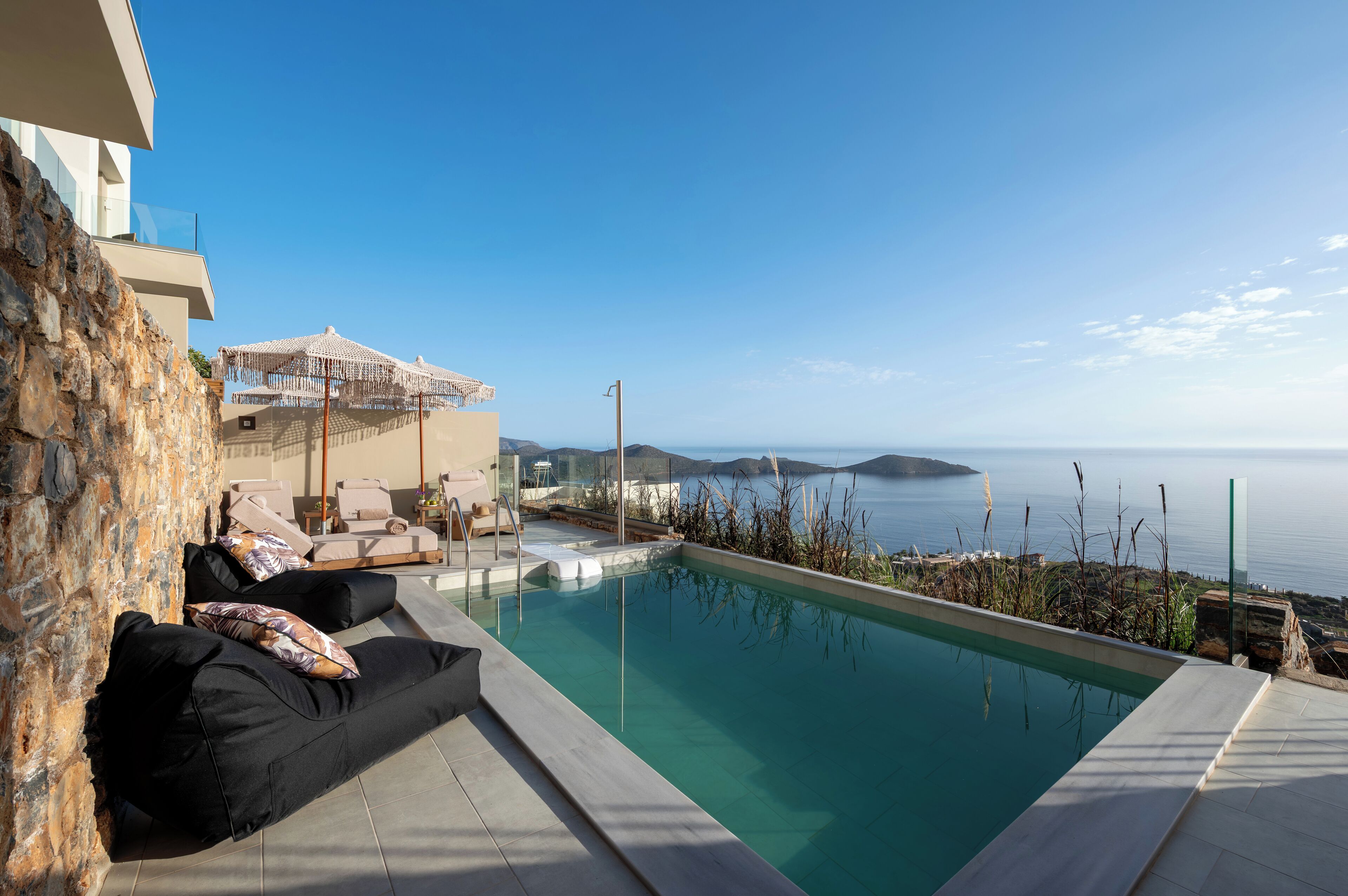 Et moderne poolområde med frit kig til havet, en stenvæg og en lounge med havudsigt.