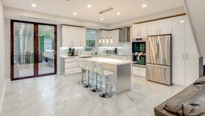 A modern kitchen with a central island, stainless steel appliances, and a sliding glass door leading to an outdoor area. - 5br Villa Rose Near Tobyhanna State Park 5 Bedroom Villa (Tobyhanna)
