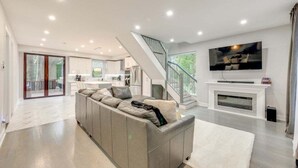 A modern living room with a grey sectional sofa, a fireplace, a TV mounted above it, and a staircase leading to another level. - 5br Villa Rose Near Tobyhanna State Park 5 Bedroom Villa (Tobyhanna)