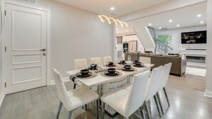 A modern dining area with a white table set for six, white chairs, and a contemporary light fixture above. - 5br Villa Rose Near Tobyhanna State Park 5 Bedroom Villa (Tobyhanna)
