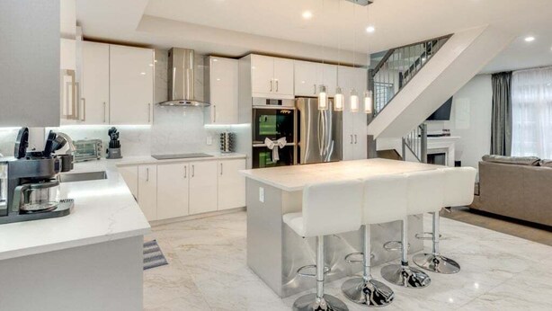 A modern kitchen with white cabinetry, stainless steel appliances, and a central island with bar stools. - 5br Villa Rose Near Tobyhanna State Park 5 Bedroom Villa (Tobyhanna)