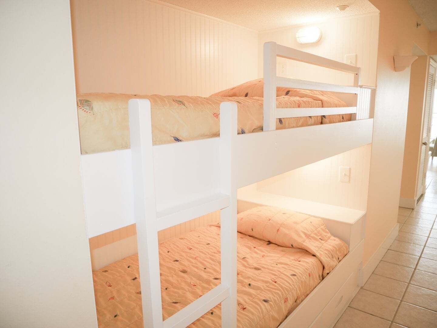 A bunk bed room with white railings and peach-colored bedding.
