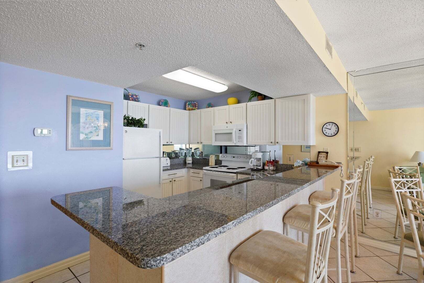 A compact kitchen with white cabinets, a granite countertop, and a bar area with stools.
