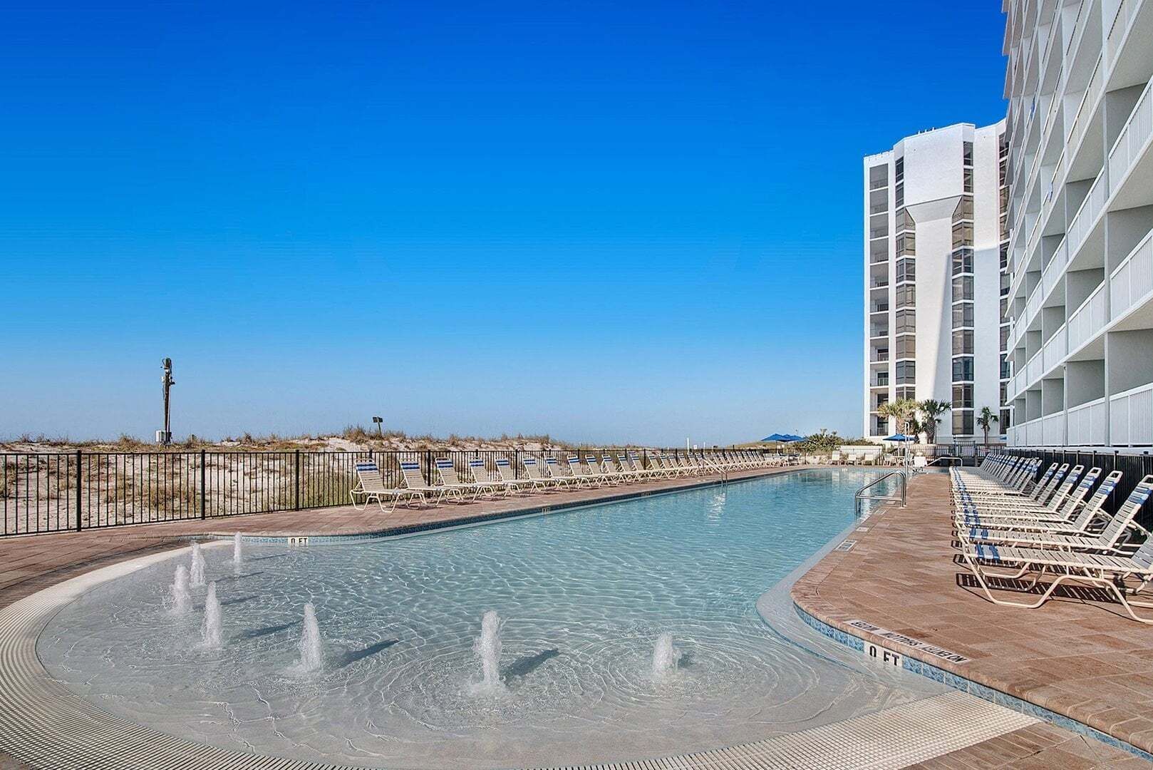 A swimming pool with lounge chairs and a building with balconies.