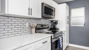 A modern kitchen with white cabinets, a stainless steel microwave, a black stove, and a tiled backsplash. - Sunny Urban Escape 3 Bedroom Home (Sarasota)