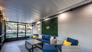 A modern lounge area with wicker furniture, a patterned rug, and a green wall with a neon sign. - Sunny Urban Escape 3 Bedroom Home (Sarasota)