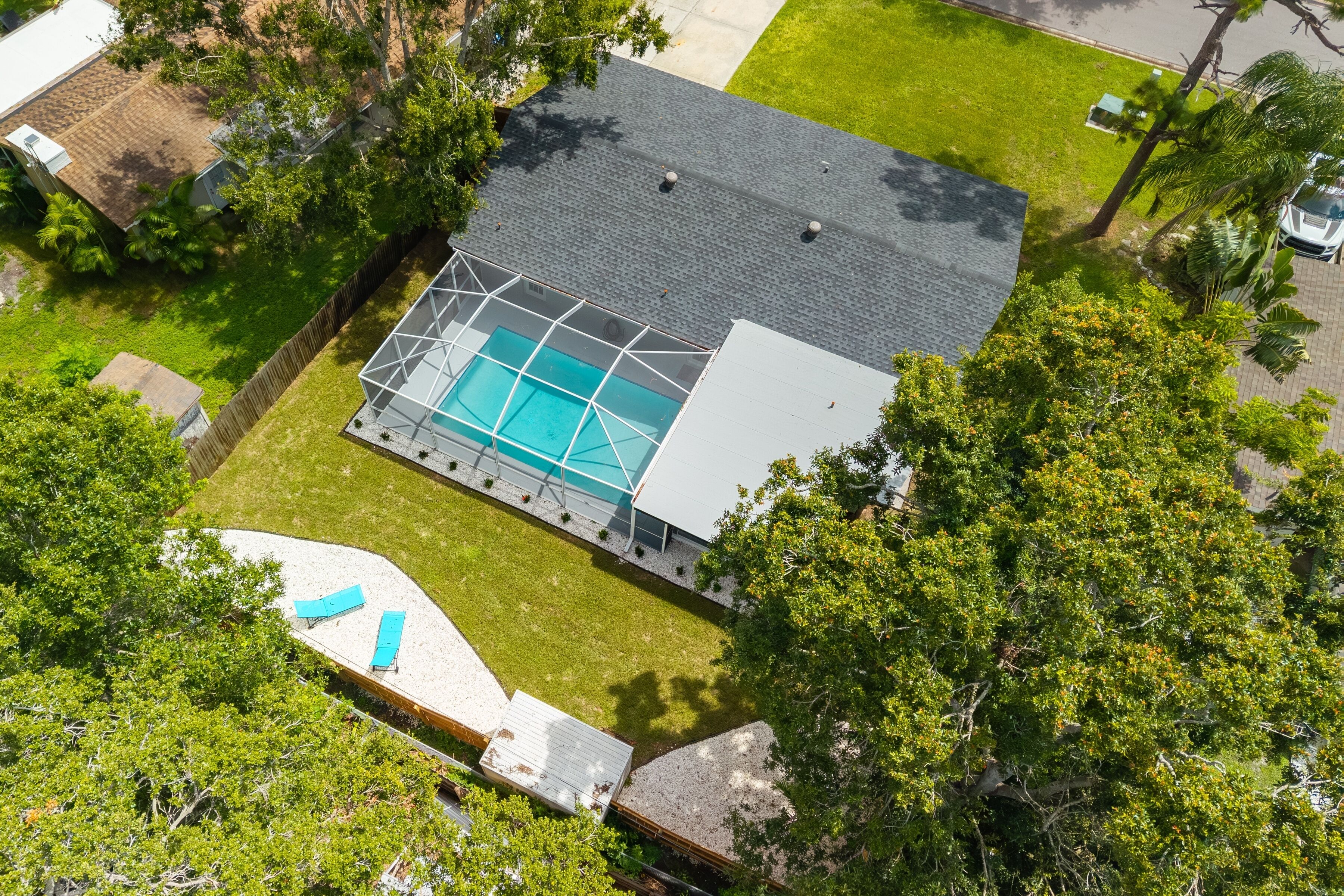 An aerial view of a house with a swimming pool, surrounded by a fenced yard and trees.