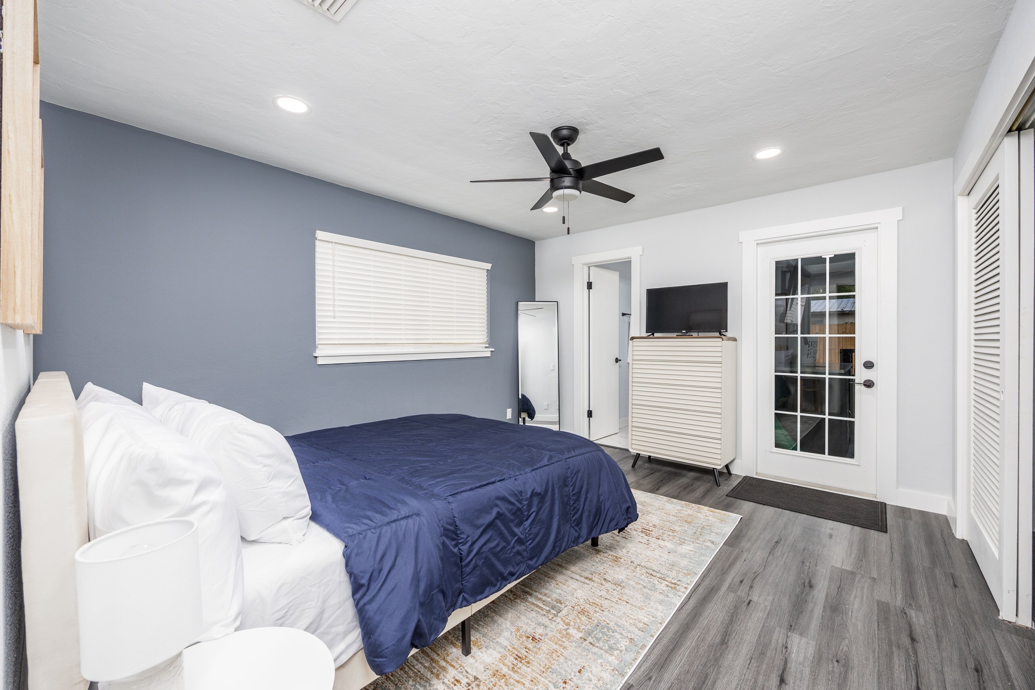 Une chambre à coucher avec un lit, un ventilateur de plafond, une porte et une fenêtre.
