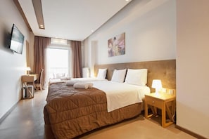 A hotel room with a large bed, a desk, a chair, a TV, and a painting on the wall. - TROKADERO BOUTIQUE HOTEL (Delphi)