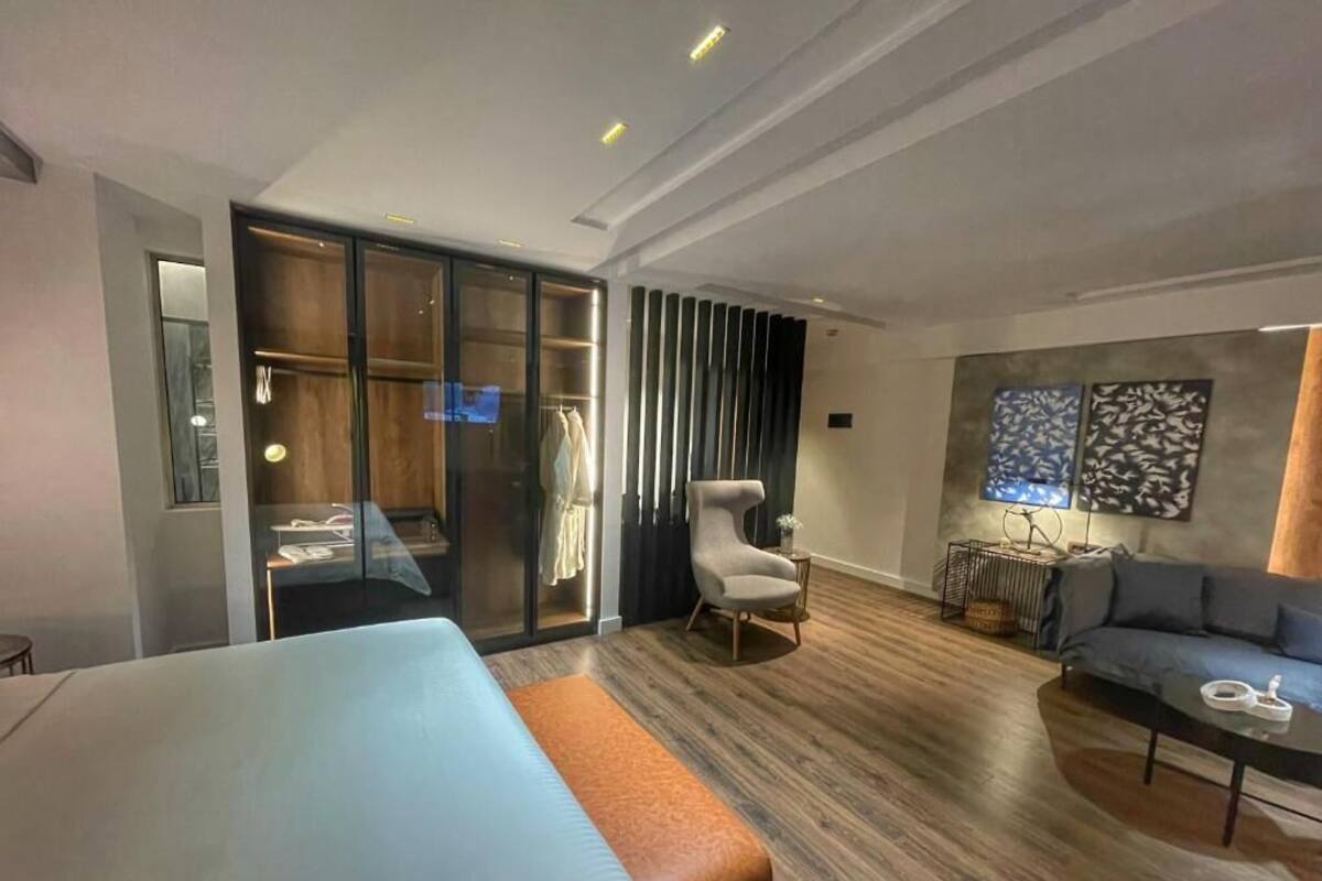 Une chambre d’hôtel moderne équipée d’un grand lit, d’un canapé, d’un fauteuil, d’un bureau et d’une armoire.