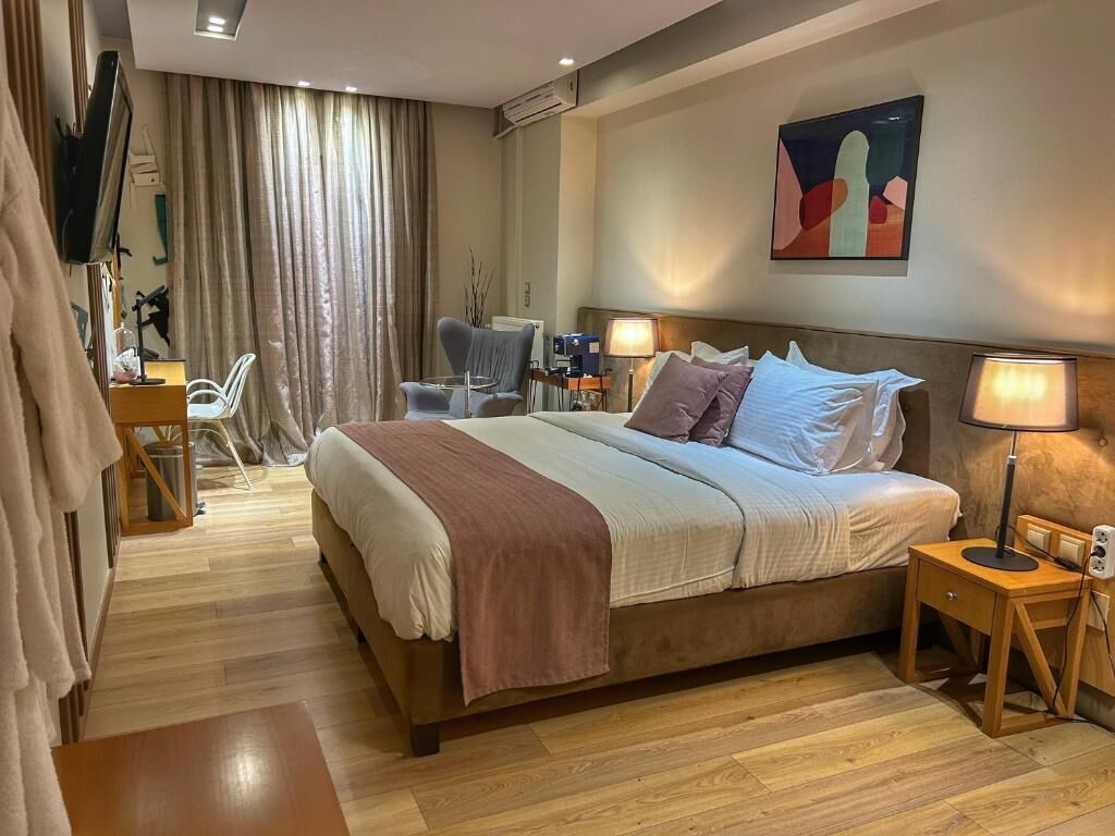 Ein modernes Hotelzimmer mit einem großen Bett, einem Schreibtisch, einem Sessel und einem Fernseher.