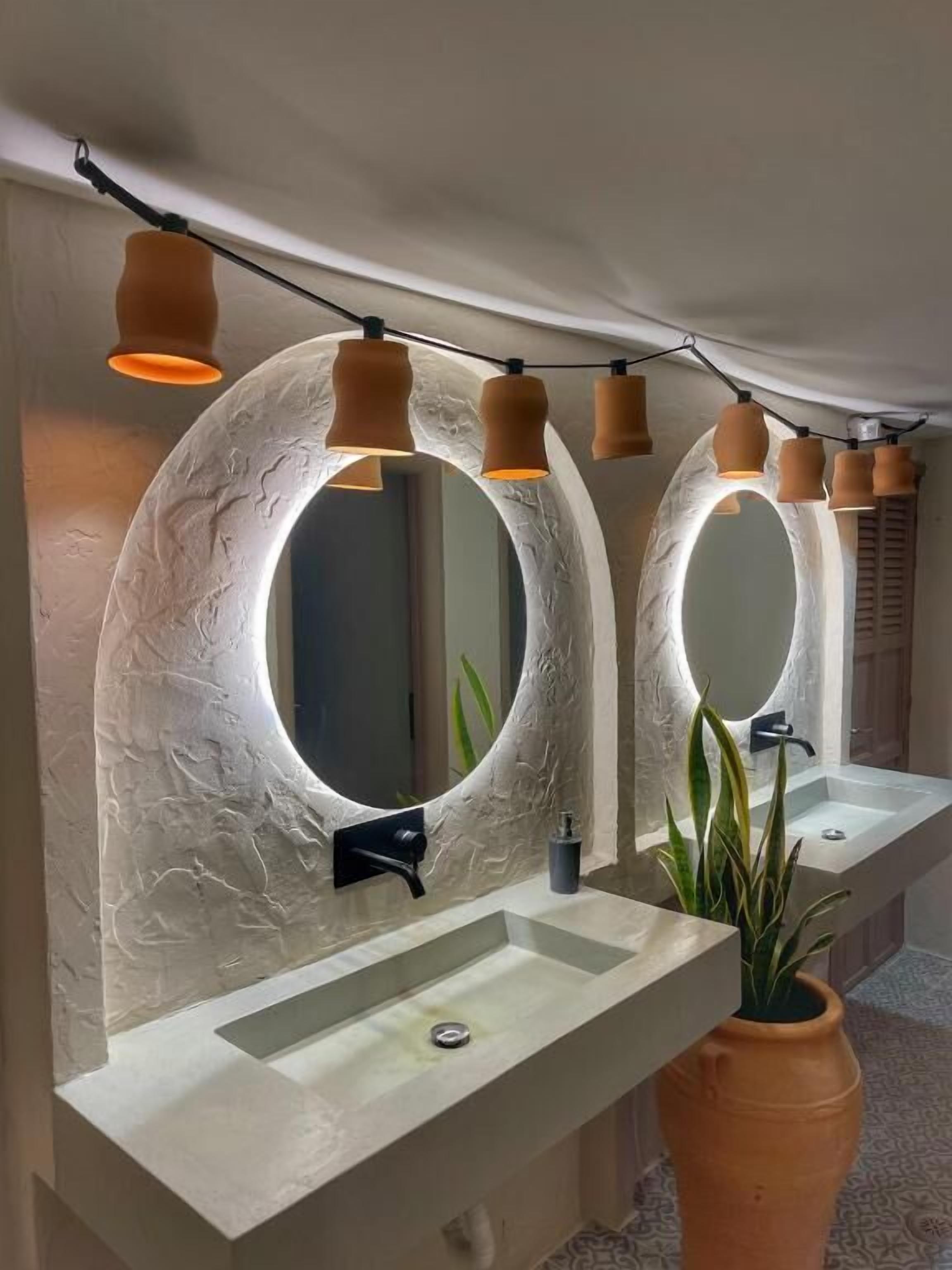 Une salle de bain avec deux grands miroirs ovales, un lavabo blanc, un robinet noir et une plante en pot.