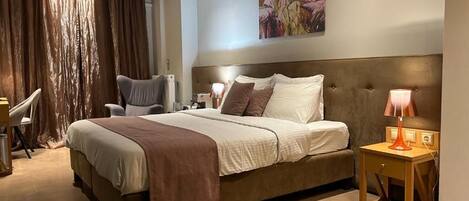 A bedroom with a large bed, a chair, a desk, and a lamp.