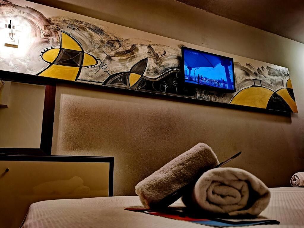 A hotel room with a large abstract painting on the wall, a television mounted above the bed, and a neatly rolled towel on the bed.
