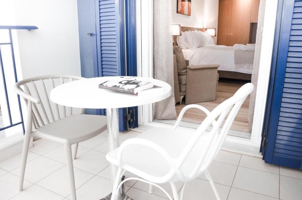Une chambre d’hôtel avec un lit, une petite table et des chaises, et une vue sur une autre chambre par une porte ouverte.