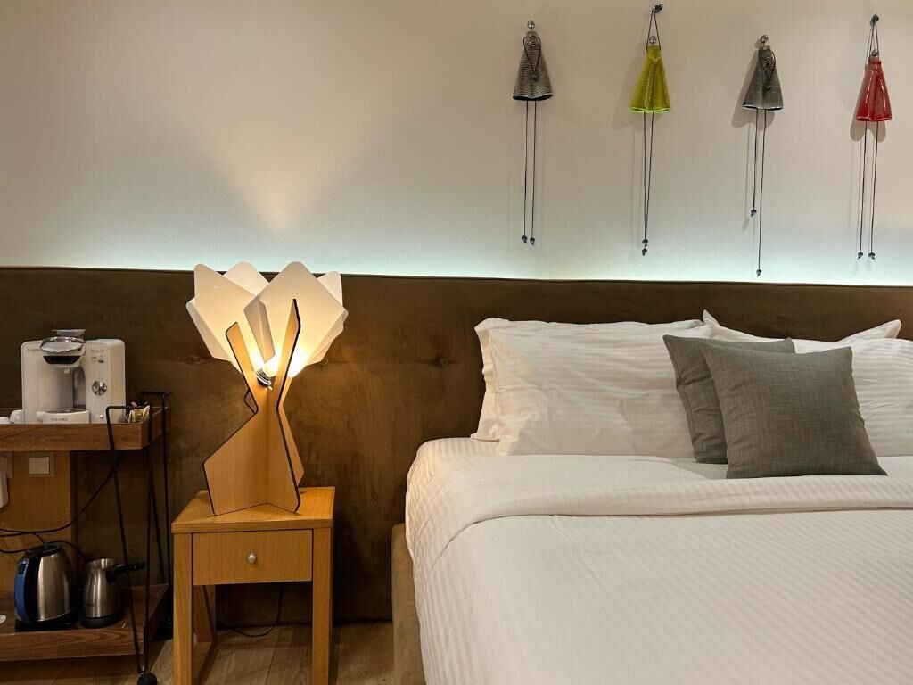 A hotel room with a bed, a bedside table with a lamp, a coffee machine, and kettles.